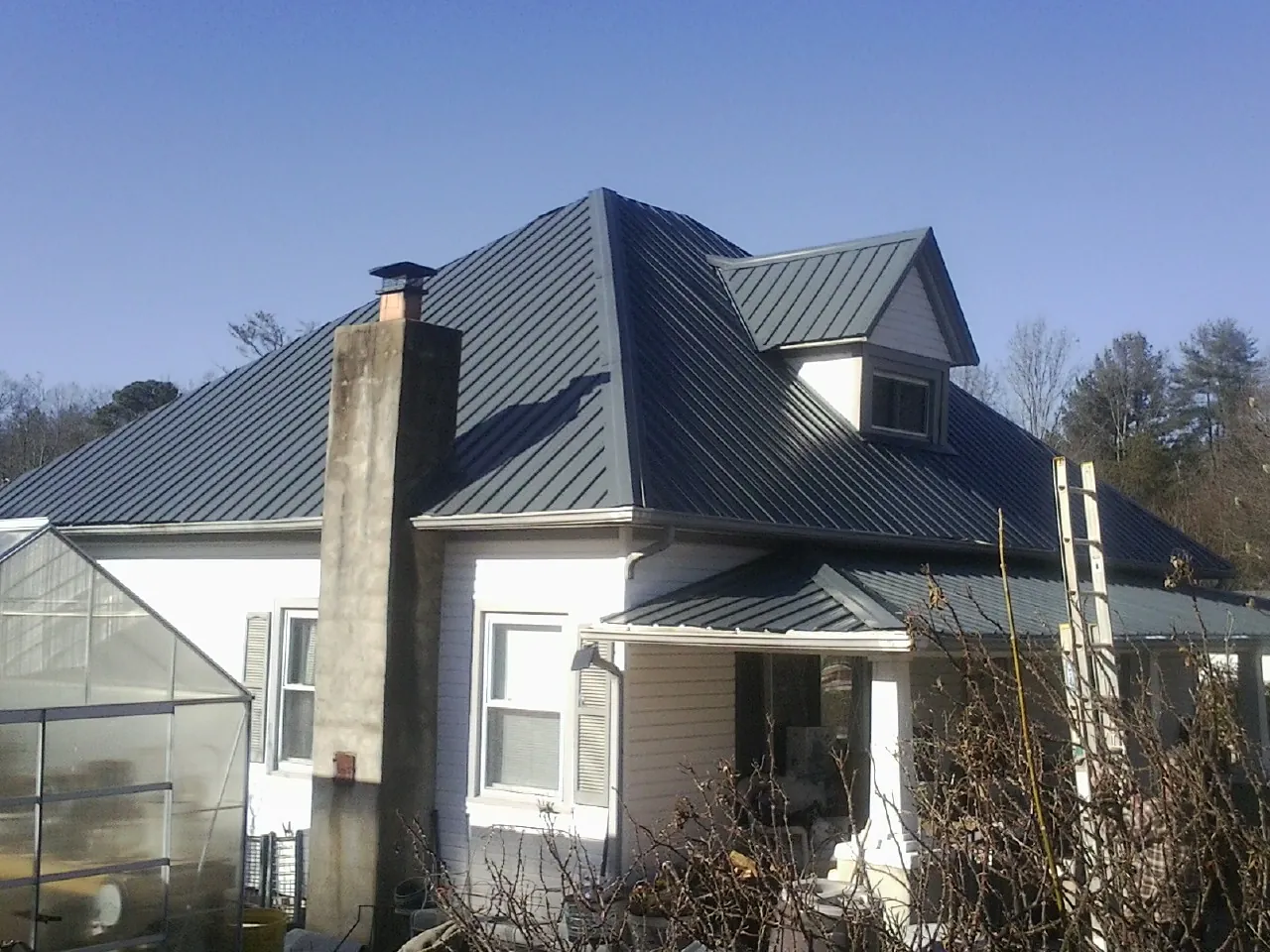 Dark blue standing seam metal roof on a white farmhouse with dormer — Slate & Tile Roof Repair by Roofing Brothers in Saint Benedict
