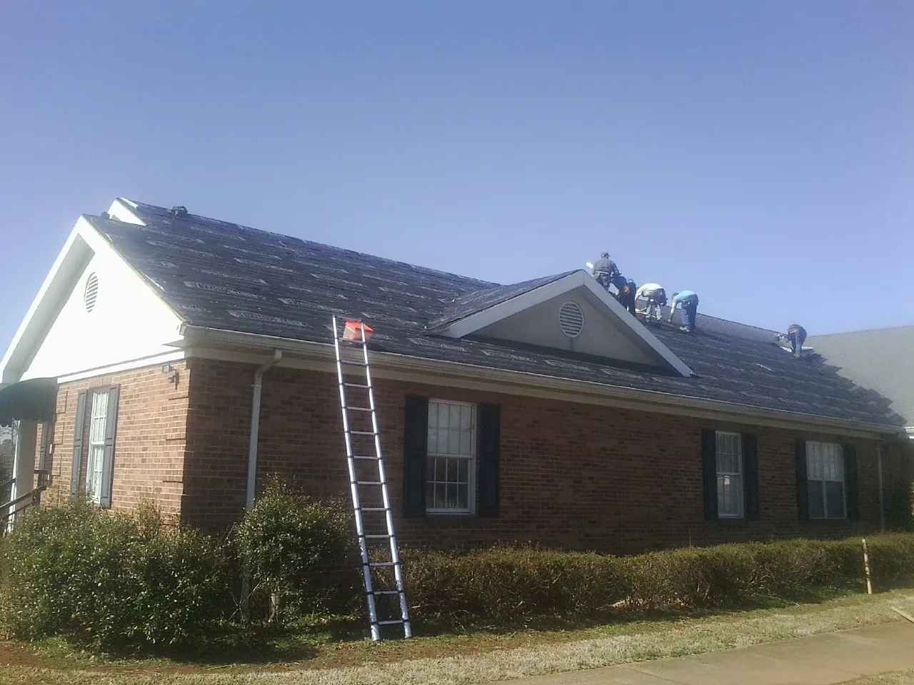 Crew tearing shingles off a brick ranch roof with a ladder set — Emergency Roof Repair work by our crew in Saint Benedict