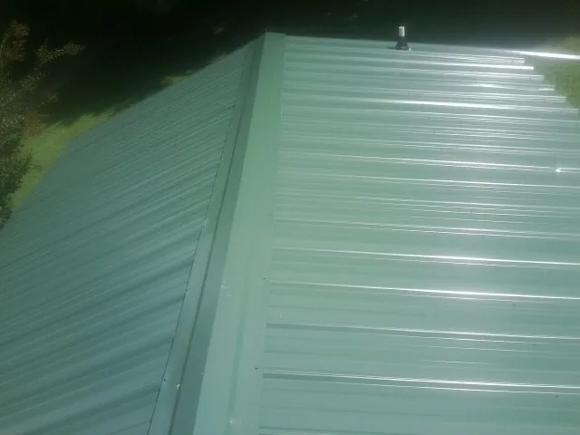 New green metal panels meeting at the ridge of a roof — Flat Roof Repair work by our crew in Saint Benedict