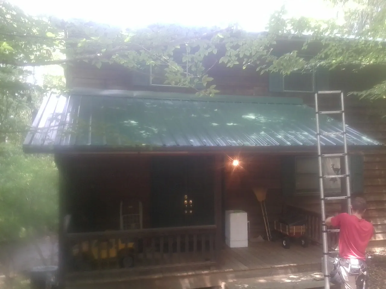 Worker on a ladder at the green porch roof of a wooded cabin in Saint Benedict