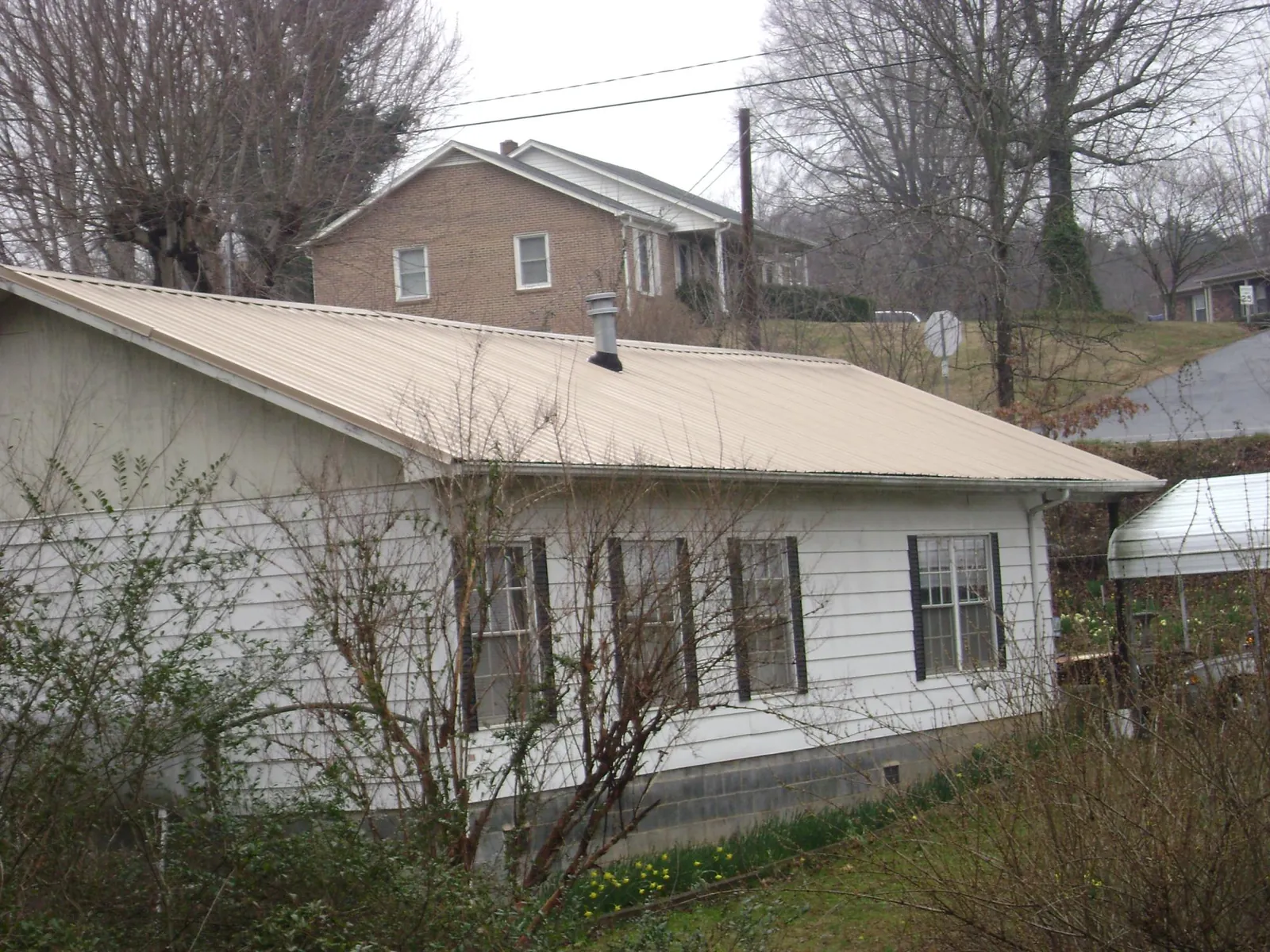 Tan metal roof on a white sided house set into a hillside — Commercial Roofing by Roofing Brothers in Saint Benedict