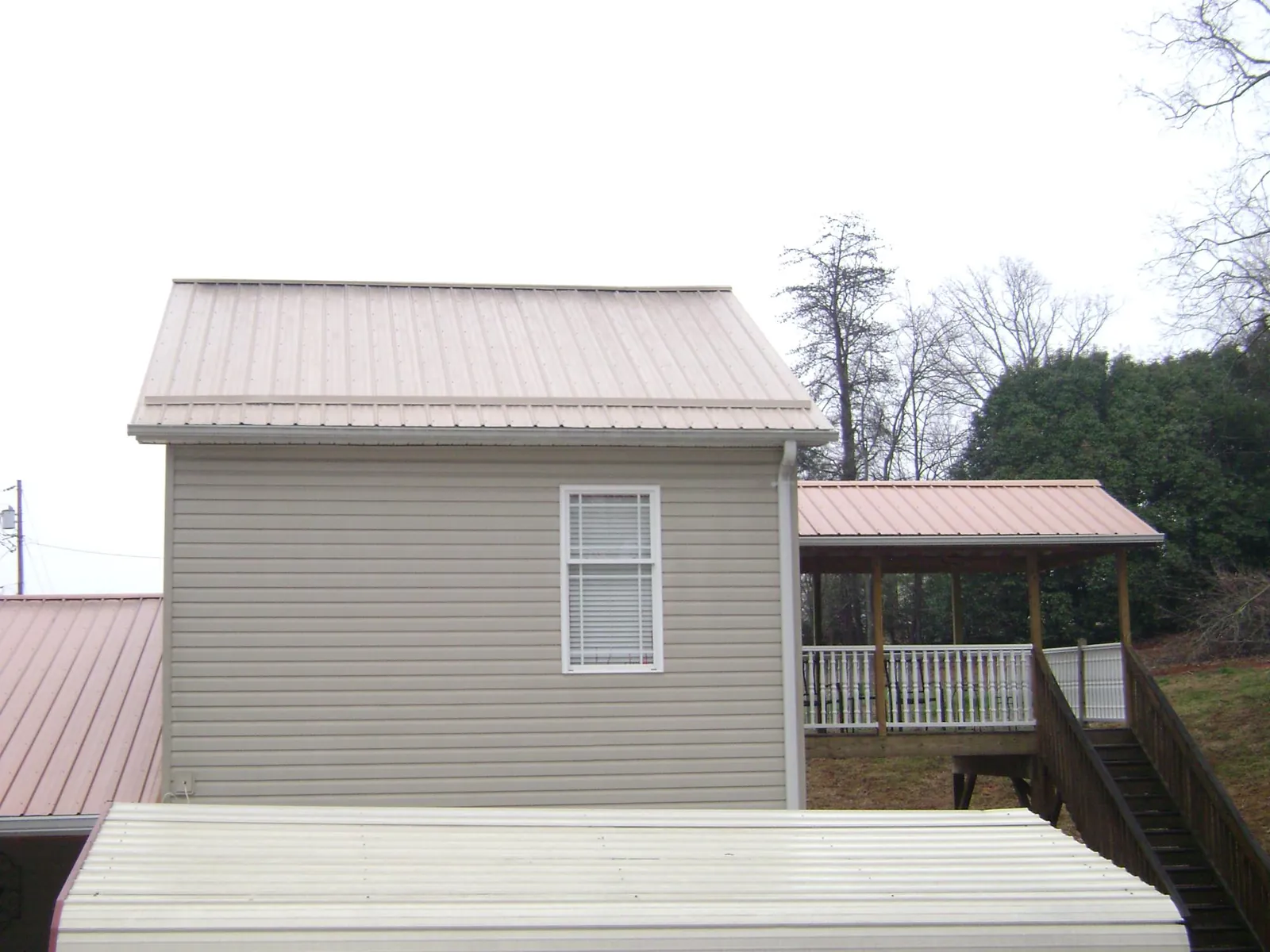 Tan metal roofs on a two story addition and attached porch, from a Roof Replacement job in Saint Benedict